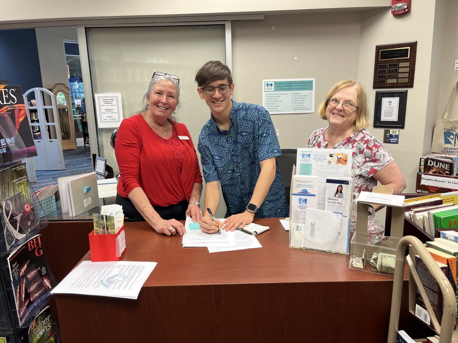 Max signing the consignment agreement with two Friends of Seminole Library volunteers at the Friends' bookstore counter.